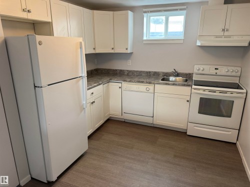 Full kitchen featuring white cabinetry, wood-finish flooring, a stainless steel sink, and a white appliance suite including a refrigerator, dishwasher, and range with overhead ventilation - 11948 132 Street, Edmonton, AB - Indoor Photo Showing Kitchen