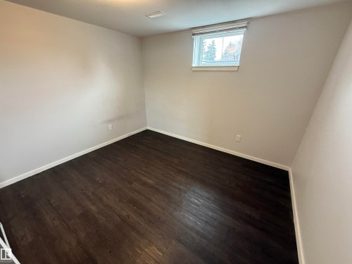 Spacious room featuring dark wood-finish flooring, light neutral walls, white trim, and a single window with blinds - 11948 132 Street, Edmonton, AB - Indoor Photo Showing Other Room