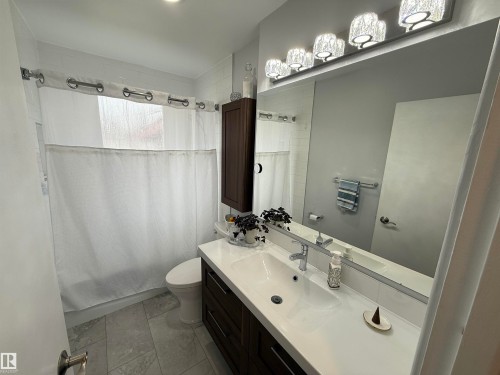 Bathroom featuring a dark wood-finish vanity with an integrated white sink, a large wall-mounted mirror, overhead vanity lighting, and light grey tile flooring - 11948 132 Street, Edmonton, AB - Indoor Photo Showing Bathroom