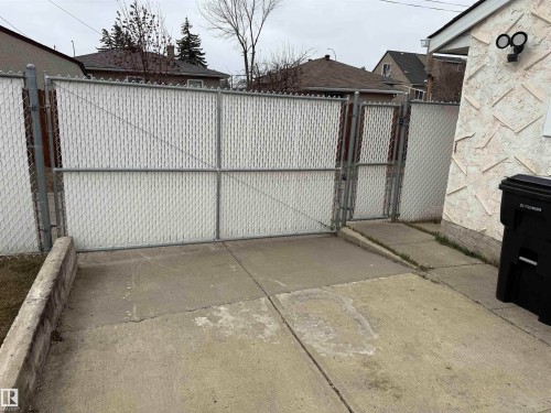 Chain-link fencing with white privacy slats and double gate entry, featuring a concrete driveway with a concrete retaining wall - 11948 132 Street, Edmonton, AB - Outdoor