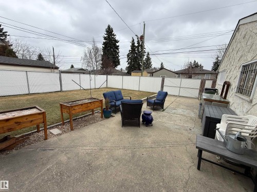 Expansive concrete patio area with a chain-link fence featuring privacy slats and a landscaped border - 11948 132 Street, Edmonton, AB - Outdoor