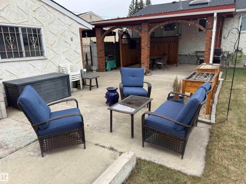 Expansive concrete patio with a covered brick archway patio area, textured exterior wall, and built-in wooden planters - 11948 132 Street, Edmonton, AB - Outdoor With Deck Patio Veranda With Exterior