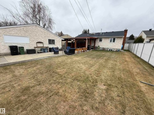 Spacious backyard featuring a large grass area, concrete patio, covered outdoor living space with a wood-finish pergola, and a stucco-finish exterior - 11948 132 Street, Edmonton, AB - Outdoor