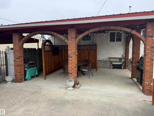 Covered patio featuring brick archways, a concrete surface, a wood privacy screen, and an exterior window - 11948 132 Street, Edmonton, AB - Outdoor