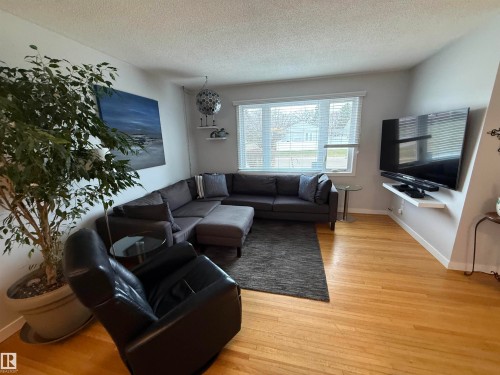 Bright living area featuring wood-finish flooring, a large window, and a wall-mounted entertainment shelf - 11948 132 Street, Edmonton, AB - Indoor Photo Showing Living Room