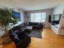 Bright living area featuring wood-finish flooring, a large window, and a wall-mounted entertainment shelf - 11948 132 Street, Edmonton, AB  - Indoor Photo Showing Living Room 