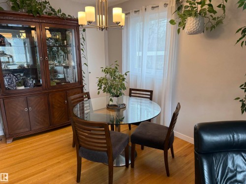 Formal dining area featuring a glass-top table, wood-finish flooring, and a contemporary chandelier - 11948 132 Street, Edmonton, AB - Indoor Photo Showing Dining Room