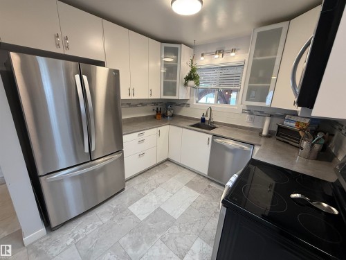 Modern kitchen featuring stainless steel appliances, light gray tile flooring, white cabinetry, and gray countertops - 11948 132 Street, Edmonton, AB - Indoor Photo Showing Kitchen