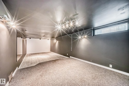 Spacious room with dark gray walls, white trim, and a combination of light-toned carpet and wood-finish flooring - 5204 112 Avenue, Edmonton, AB - Indoor Photo Showing Other Room