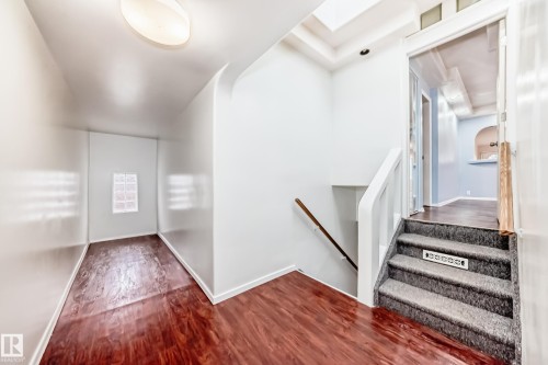 Entryway featuring wood-finish flooring, a glass block window, and a carpeted staircase with a white railing and wood handrail - 5204 112 Avenue, Edmonton, AB - Indoor Photo Showing Other Room