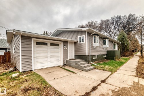 Split-level residence featuring grey horizontal siding, a white garage door with upper window inserts, and concrete steps leading to the main entrance - 5204 112 Avenue Nw, Edmonton, AB - Outdoor