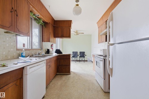 Kitchen featuring wood cabinetry, white countertops, mosaic tile backsplash, and a double basin sink - 11211 77 Avenue, Edmonton, AB - Indoor Photo Showing Kitchen With Double Sink