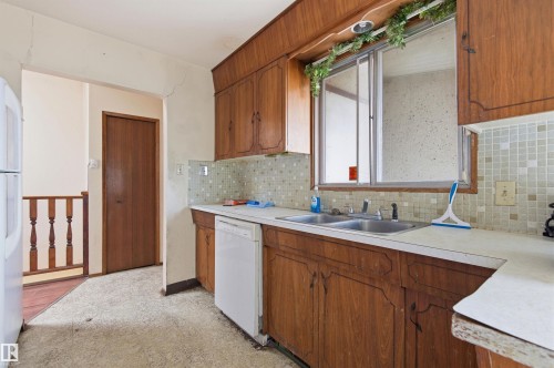 Kitchen featuring wood cabinetry, a double basin stainless steel sink, a dishwasher, a window, and a tile backsplash - 11211 77 Avenue, Edmonton, AB - Indoor Photo Showing Kitchen With Double Sink