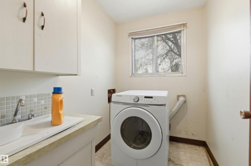 Utility room featuring a window, built-in cabinetry, a utility sink with mosaic tile backsplash, and a light-toned countertop - 11211 77 Avenue, Edmonton, AB - Indoor Photo Showing Laundry Room