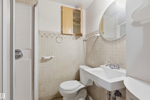 Bathroom featuring a tiled shower enclosure, pedestal sink, wall-mounted mirror, square tile wainscoting, and an upper storage cabinet - 11211 77 Avenue, Edmonton, AB - Indoor Photo Showing Bathroom