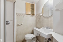 Bathroom featuring a tiled shower enclosure, pedestal sink, wall-mounted mirror, square tile wainscoting, and an upper storage cabinet - 