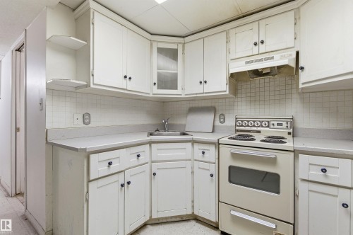 Kitchen featuring white cabinetry, a corner sink, a wall-mounted range hood, a four-burner electric range, and a tile backsplash - 11211 77 Avenue, Edmonton, AB - Indoor Photo Showing Kitchen
