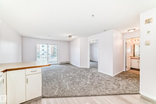Open-concept living space with light gray carpet, white walls, and a sliding glass door leading to a balcony - 218 10535 122 Street, Edmonton, AB - Indoor Photo Showing Kitchen