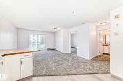 Open-concept living space with light gray carpet, white walls, and a sliding glass door leading to a balcony - 