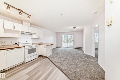 Open concept living area featuring a kitchen with white cabinetry, a built-in dishwasher, and a white electric range - 218 10535 122 Street, Edmonton, AB - Indoor Photo Showing Kitchen