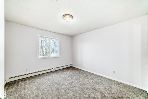 Bright interior space featuring a window with exterior tree scenery, plush gray carpeting, white walls, and a ceiling-mounted light fixture - 218 10535 122 Street, Edmonton, AB - Indoor Photo Showing Other Room