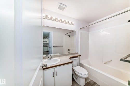 Bathroom featuring a white vanity with an integrated sink, a light-colored countertop, and a large wall mirror - 218 10535 122 Street, Edmonton, AB - Indoor Photo Showing Bathroom