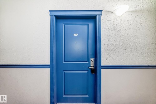 Vibrant blue paneled door with traditional molding, featuring a contemporary handle set and visible house number - 218 10535 122 Street, Edmonton, AB - 