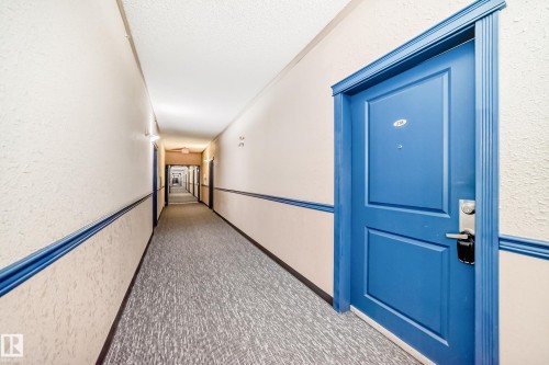 Long interior hallway with textured wallpaper and crown molding - 218 10535 122 Street, Edmonton, AB - Indoor Photo Showing Other Room