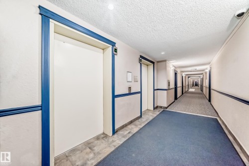 Hallway featuring two elevators with blue trim, recessed lighting, and a combination of blue and gray carpeting - 218 10535 122 Street, Edmonton, AB -  With Exterior