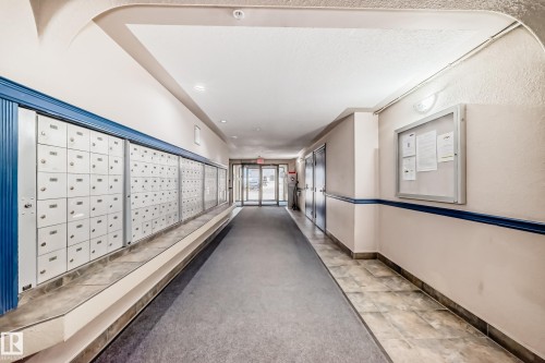 Hallway featuring a wall of private mailboxes, carpet flooring, tile flooring, and wall-mounted lighting fixtures - 218 10535 122 Street, Edmonton, AB - Indoor Photo Showing Other Room