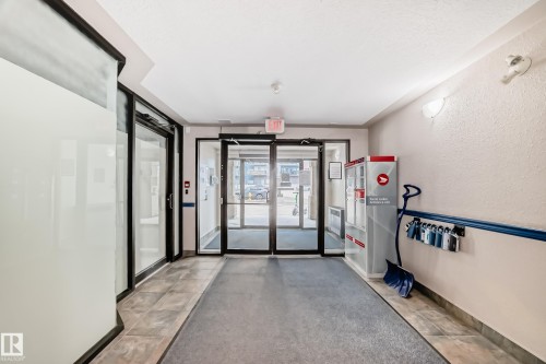 Entryway featuring automatic glass doors with black framing, tile flooring, and textured wall finishes - 218 10535 122 Street, Edmonton, AB - Indoor Photo Showing Other Room