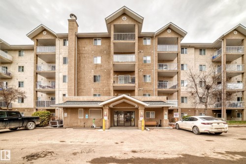 Multi-story building featuring individual balconies with white railings, a prominent central entrance with an awning, and a textured stucco exterior - 218 10535 122 Street, Edmonton, AB - Outdoor With Facade