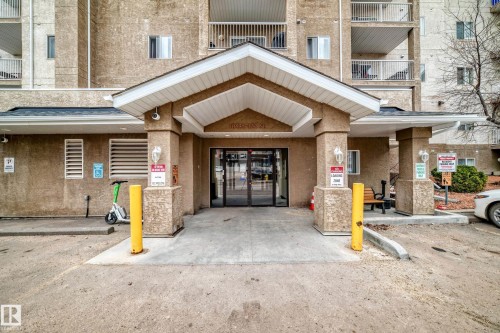 Building entrance featuring an overhead portico with soffit lighting and a dark shingle roof - 218 10535 122 Street, Edmonton, AB - Outdoor