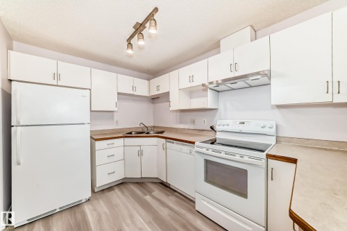 Kitchen featuring white cabinetry, a double basin sink, white range, white refrigerator, and wood-finish flooring - 218 10535 122 Street, Edmonton, AB - Indoor Photo Showing Kitchen With Double Sink