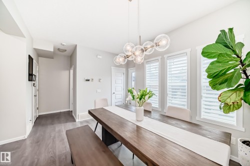 Dining area featuring a contemporary linear chandelier with clear glass globes, wood-finish flooring, and multiple windows with white blinds - 3278 Cherry Crescent, Edmonton, AB - Indoor Photo Showing Dining Room