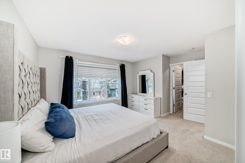 Carpeted bedroom featuring a large window with blinds and dark curtains, a ceiling-mounted light fixture, light gray wall paint, and a white paneled door - 3278 Cherry Crescent, Edmonton, AB - Indoor Photo Showing Bedroom