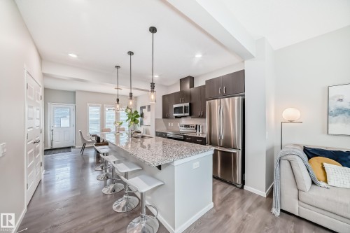 Open-concept kitchen featuring an oversized island with a granite countertop, dark wood-finish cabinetry, and stainless steel appliances - 3278 Cherry Crescent, Edmonton, AB - Indoor Photo Showing Kitchen With Upgraded Kitchen