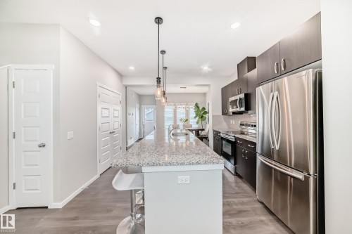 Contemporary kitchen featuring dark wood-finish cabinetry, stainless steel appliances, and a spacious island with a light speckled countertop - 3278 Cherry Crescent, Edmonton, AB - Indoor Photo Showing Kitchen With Upgraded Kitchen