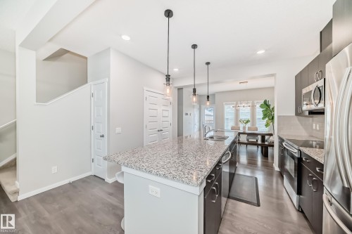 Spacious kitchen featuring a large island with a speckled countertop, stainless steel appliances, dark wood-finish cabinetry, and contemporary pendant lighting - 3278 Cherry Crescent, Edmonton, AB - Indoor Photo Showing Kitchen With Upgraded Kitchen