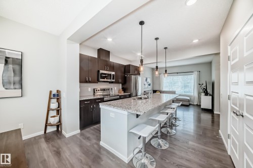 Open-concept kitchen featuring dark wood cabinetry, stainless steel appliances, and a light granite island with pendant lighting - 3278 Cherry Crescent, Edmonton, AB - Indoor Photo Showing Kitchen With Upgraded Kitchen