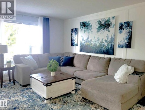Living area featuring a large window with white blinds, white wainscoting on accent wall, and wood-finish flooring beneath a patterned area rug - 144 Kirpatrick Way, Leduc, AB - Indoor Photo Showing Living Room