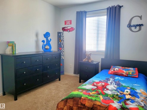 Carpeted room featuring a window with blinds and gray curtains, a dark wood-finish dresser with nine drawers, and a coordinating nightstand with two drawers - 144 Kirpatrick Way, Leduc, AB - Indoor Photo Showing Bedroom