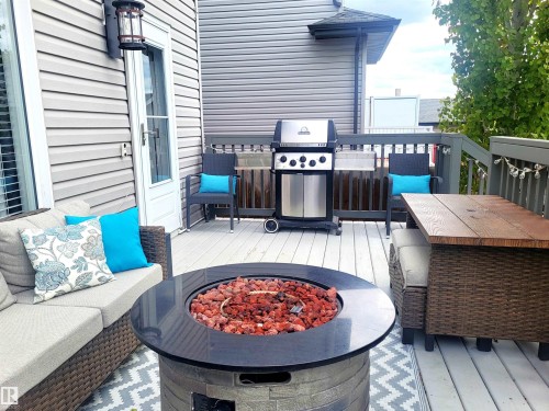 Exterior deck featuring a built-in fire pit, gray siding, white deck railing, and a patio door with an exterior light fixture - 144 Kirpatrick Way, Leduc, AB - Outdoor With Deck Patio Veranda With Exterior
