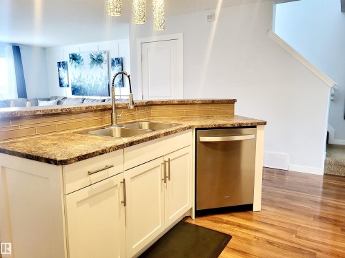 Kitchen island featuring a double basin stainless steel sink with a pull-down faucet, a stainless steel dishwasher, and white cabinetry with brushed nickel hardware - 144 Kirpatrick Way, Leduc, AB - Indoor Photo Showing Kitchen With Double Sink