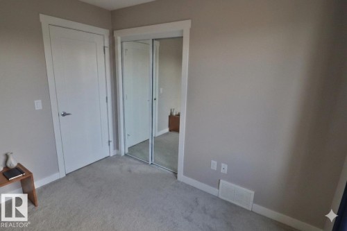 Neutral tone wall paint with white trim, featuring a mirrored sliding closet door, white interior door, and grey carpet flooring - 81 446 Allard Blvd, Edmonton, AB - Indoor Photo Showing Other Room