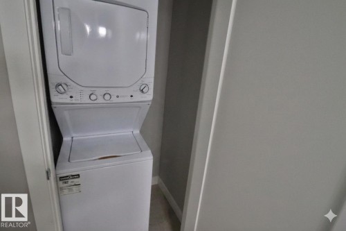 Stacked white washer and dryer unit within a dedicated closet space, featuring control knobs and a top-loading washer design - 81 446 Allard Blvd, Edmonton, AB - Indoor Photo Showing Laundry Room