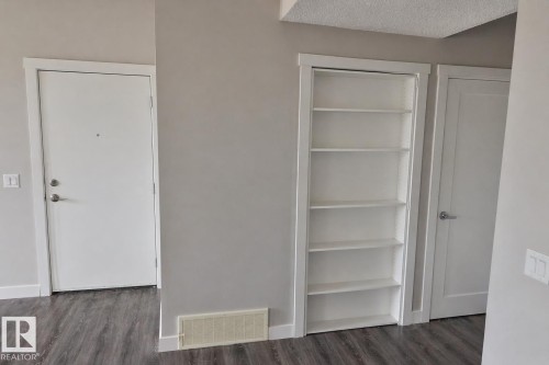 Built-in shelving unit with white finish, complementing the light gray wall paint and dark wood-finish flooring - 81 446 Allard Blvd, Edmonton, AB - Indoor Photo Showing Other Room