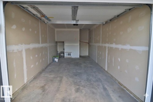 Concrete flooring garage with drywall-ready walls and an overhead door mechanism - 81 446 Allard Blvd, Edmonton, AB - Indoor Photo Showing Garage