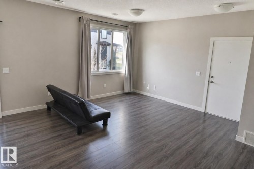 Spacious interior featuring wood-finish flooring, neutral paint palette, ample natural light from a large window, white trim throughout, and ceiling-mounted light fixtures - 81 446 Allard Blvd, Edmonton, AB - Indoor