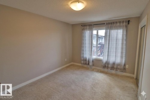 Neutral-toned room with plush carpeting, a large window, and a mirrored closet door - 81 446 Allard Blvd, Edmonton, AB - Indoor Photo Showing Other Room